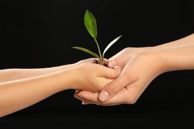Photo of Woman and her child holding soil with green plant in hands on black background. Family concept