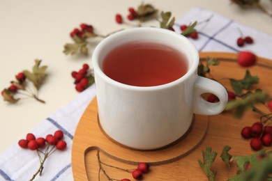 Photo of Cup with hawthorn tea and berries on beige table, closeup