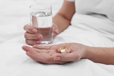 Photo of Woman with vitamin pills and glass of water in bed, closeup