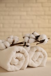 Photo of Rolled terry towels and cotton branch on white table near brick wall indoors, space for text
