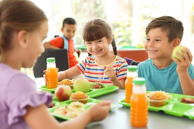 Photo of Children sitting at table and eating healthy food during break at school