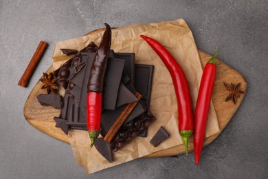 Photo of Red hot chili peppers and pieces of dark chocolate with spices on grey table, flat lay
