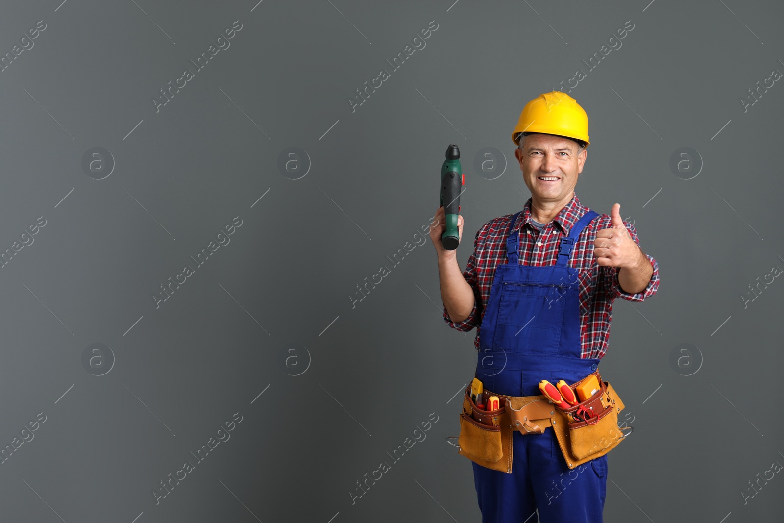 Photo of Electrician with drill wearing uniform on gray background. Space for text