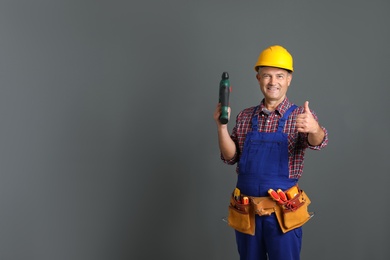Photo of Electrician with drill wearing uniform on gray background. Space for text