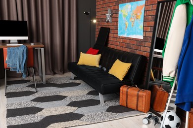 Stylish teenager's room with black sofa, computer, suitcase and world map on brick wall