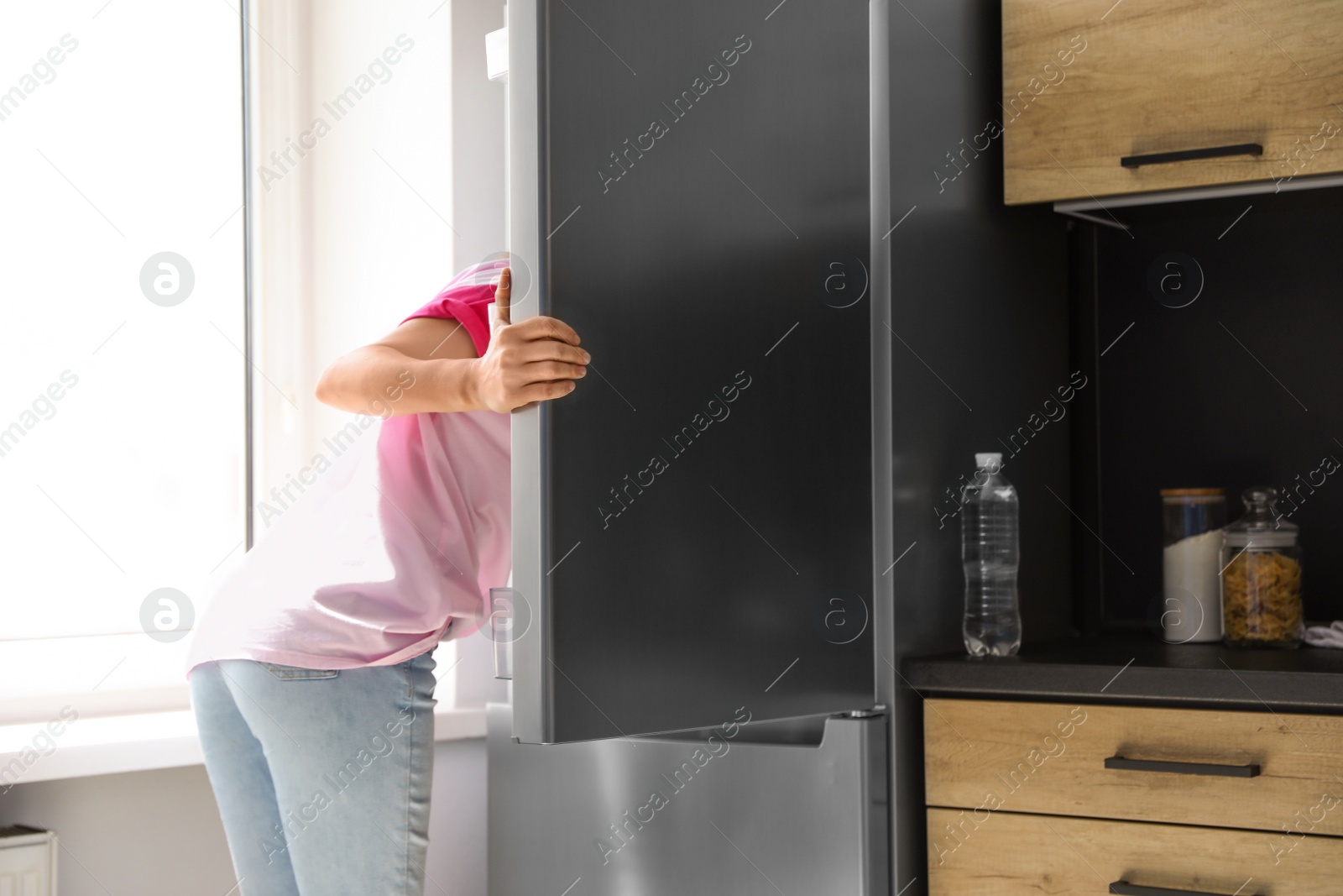 Photo of Woman looking into refrigerator full of products in kitchen