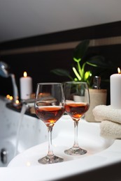 Photo of Bathtub with glasses of wine and candles indoors. Romantic atmosphere