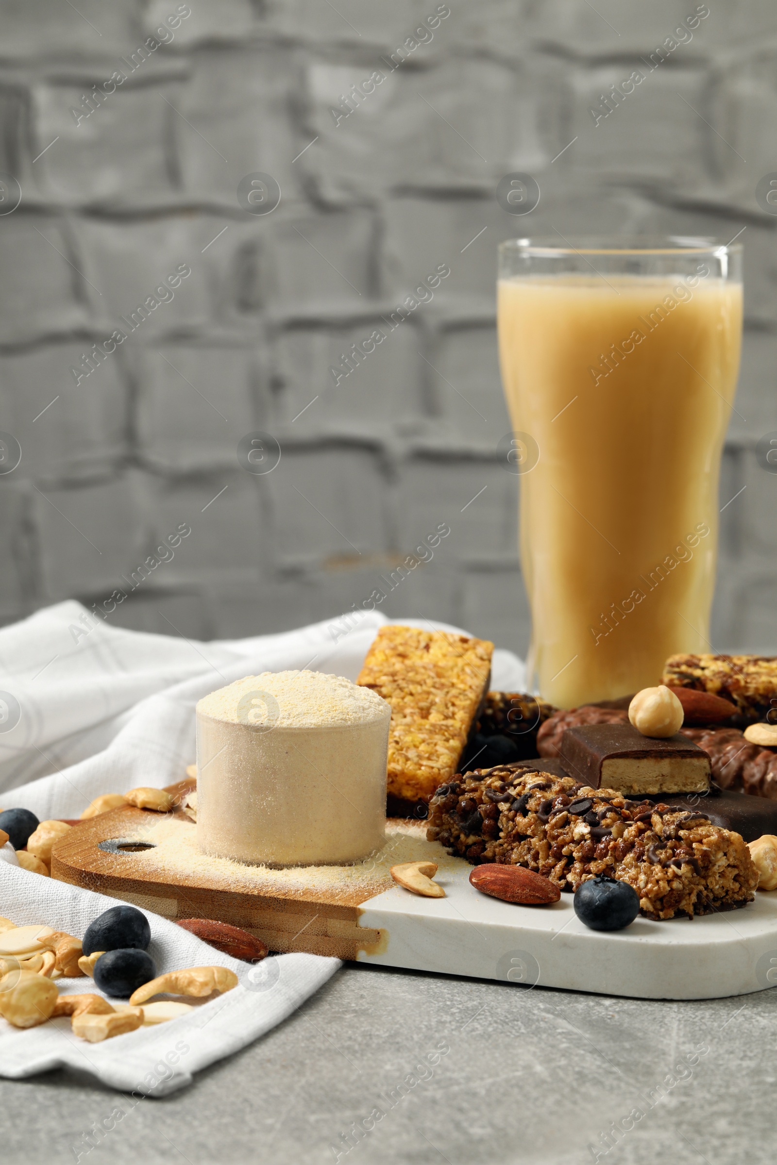 Photo of Different energy bars, nuts, blueberries, protein cocktail and powder on grey table