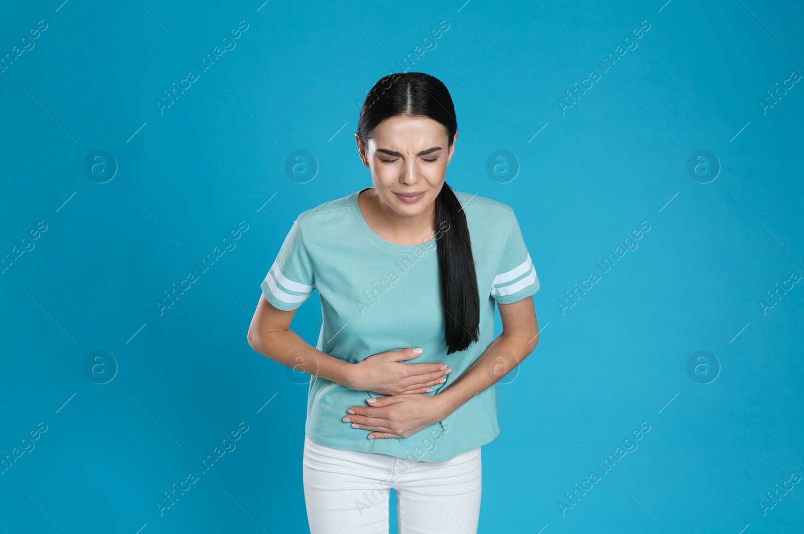 Photo of Woman suffering from stomach ache on light blue background. Food poisoning