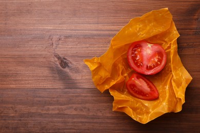 Photo of Slices of fresh tomato in beeswax food wrap on wooden table, top view. Space for text