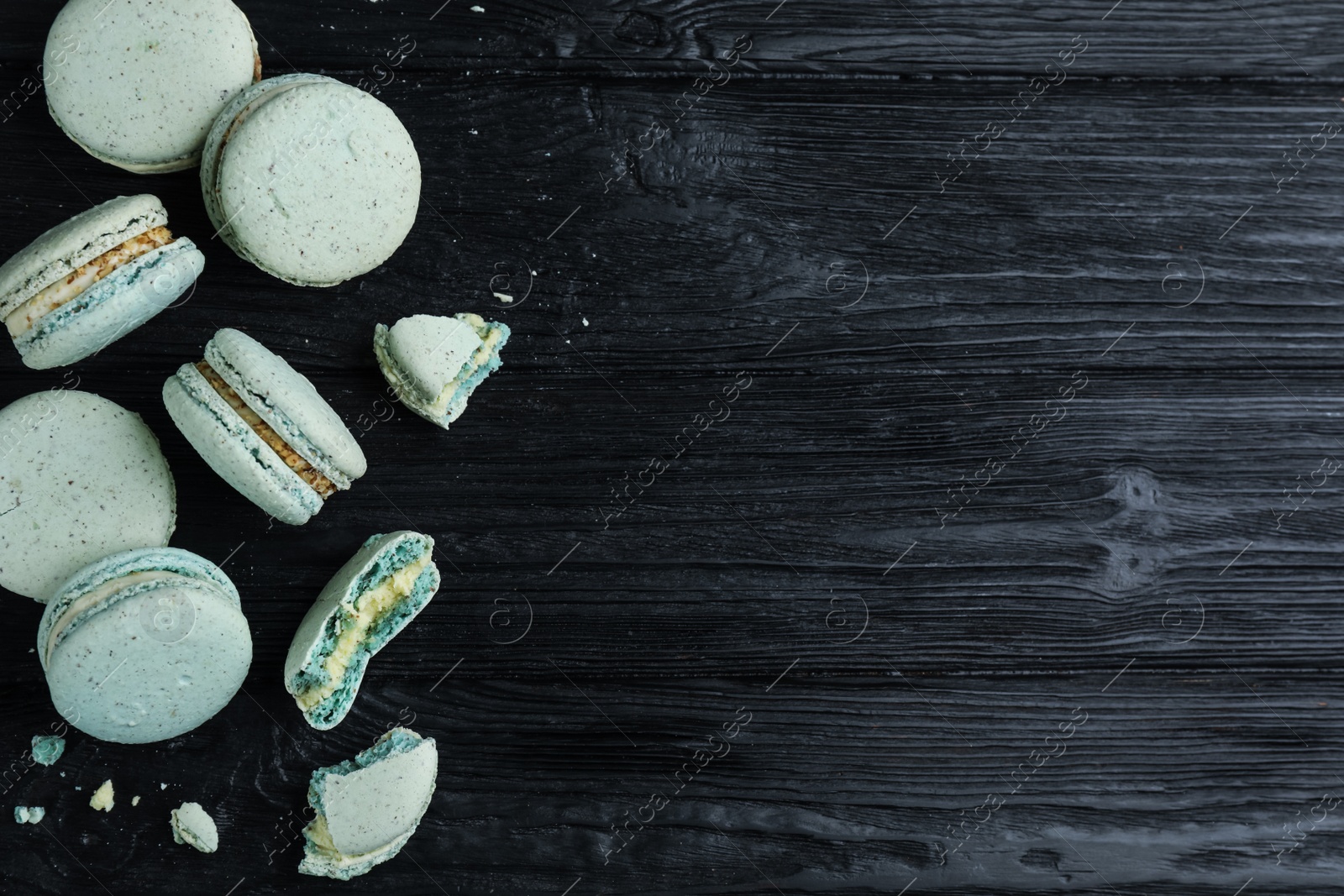 Photo of Delicious light blue macarons on black wooden table, flat lay. Space for text