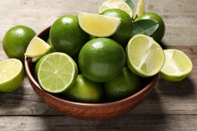 Photo of Tasty ripe limes in bowl on wooden table, closeup