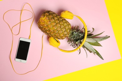 Pineapple with headphones and smartphone on color background, top view