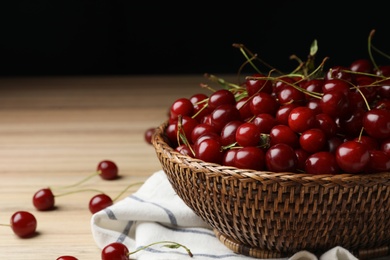 Photo of Wicker bowl of delicious cherries with towel on wooden table, space for text