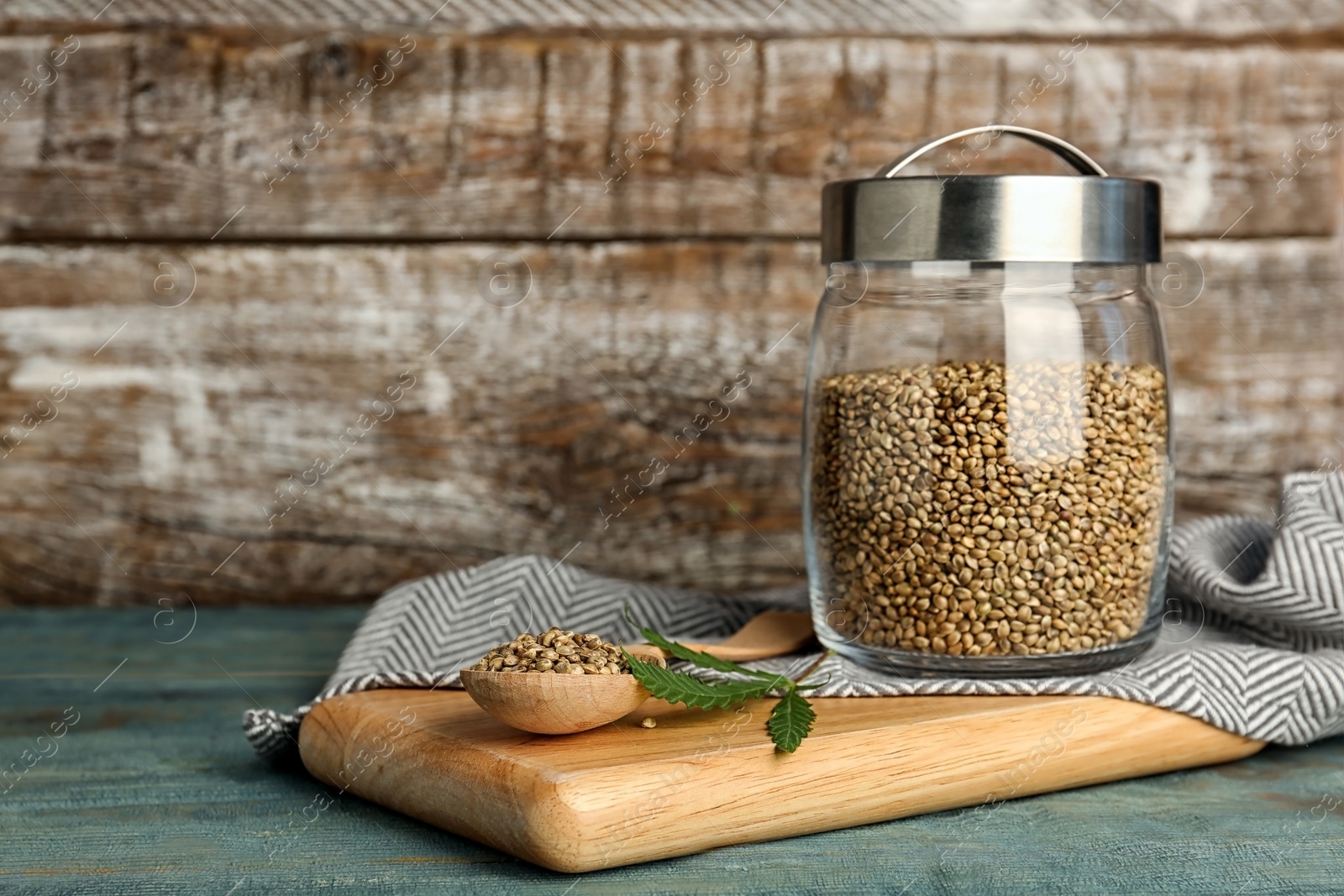 Photo of Jar and spoon of hemp seeds on table against wooden wall