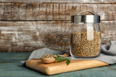 Photo of Jar and spoon of hemp seeds on table against wooden wall
