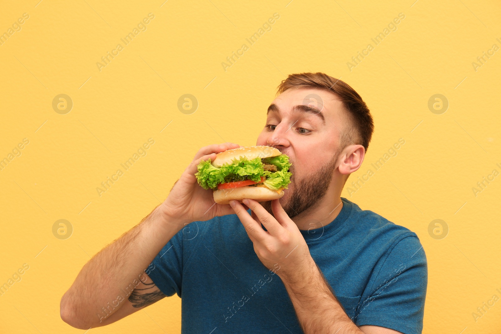 Photo of Young man eating tasty burger on color background. Space for text