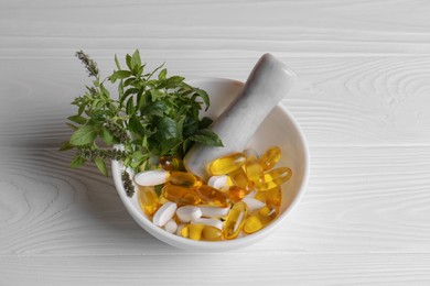 Mortar with fresh green herbs and pills on white wooden table, above view