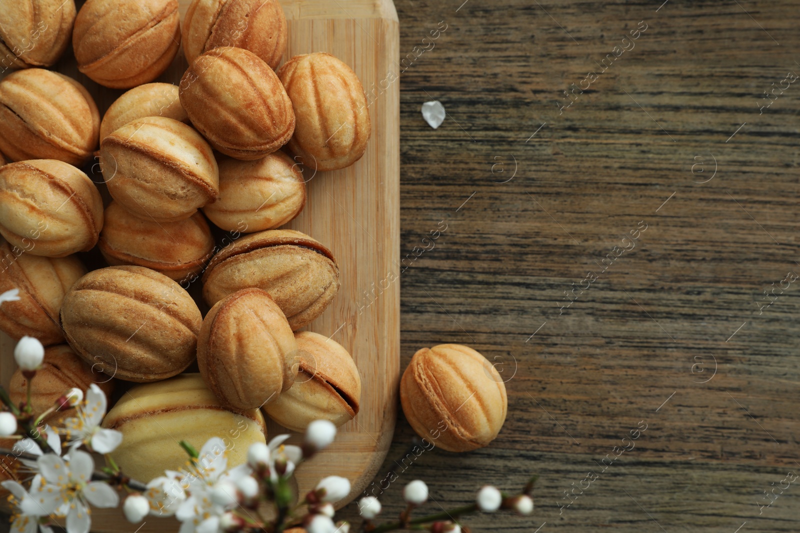 Photo of Delicious walnut shaped cookies with filling and cherry branch on wooden table, flat lay and space for text. Homemade popular biscuits from childhood