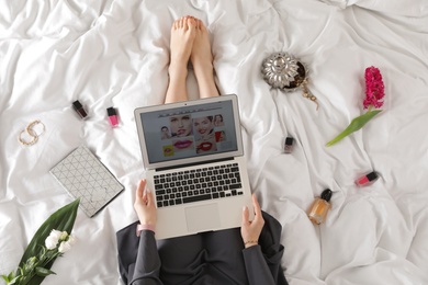 Woman and laptop with beauty blogger site on bed, top view