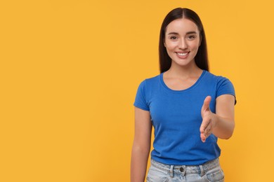 Photo of Happy young woman welcoming and offering handshake on yellow background, space for text