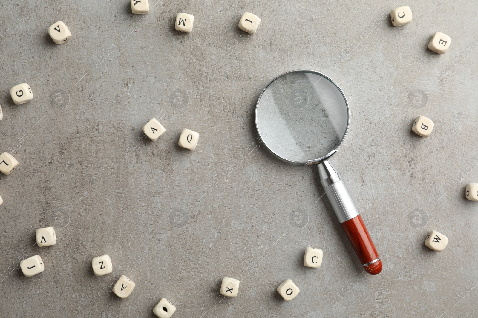 Photo of Magnifier glass and cubes with letters on light grey stone background, flat lay. Find keywords concept