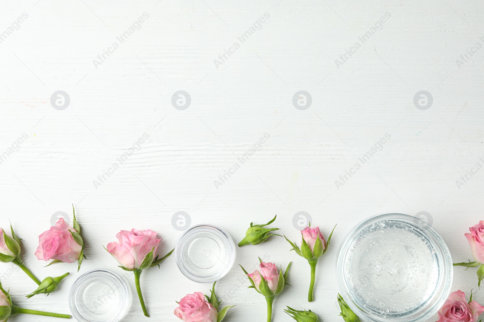 Photo of Flat lay composition with cosmetic gel and beautiful flowers on white wooden table. Space for text