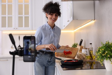 Photo of Smiling food blogger cooking while recording video in kitchen