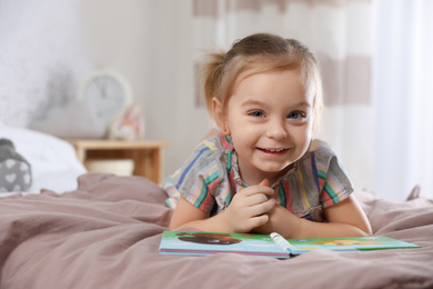 Photo of Cute little girl with book on bed at home