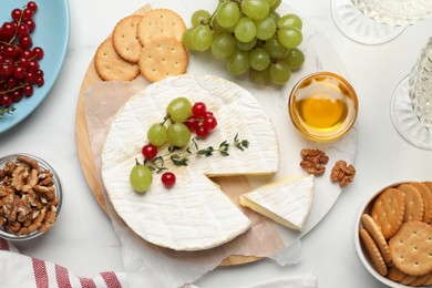 Photo of Brie cheese served with honey, berries and crackers on white table, flat lay