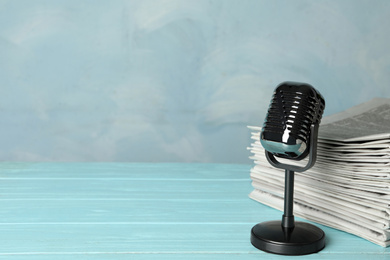 Newspapers and vintage microphone on light blue wooden table, space for text. Journalist's work
