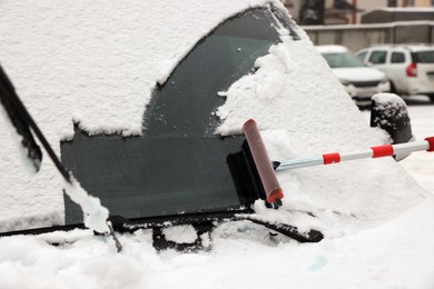 Cleaning car windshield from snow with squeegee outdoors