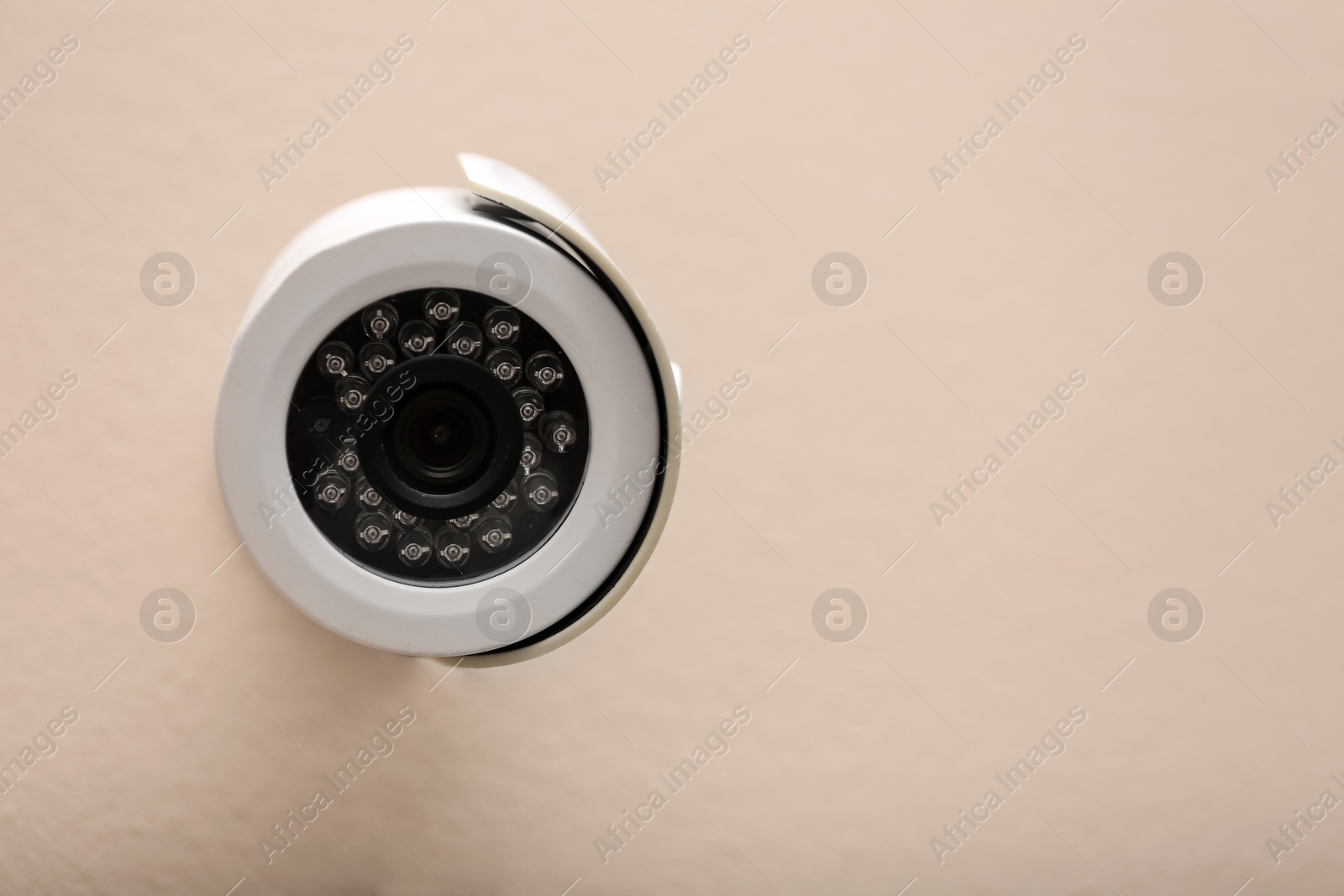 Photo of Modern CCTV security camera on beige wall. Space for text