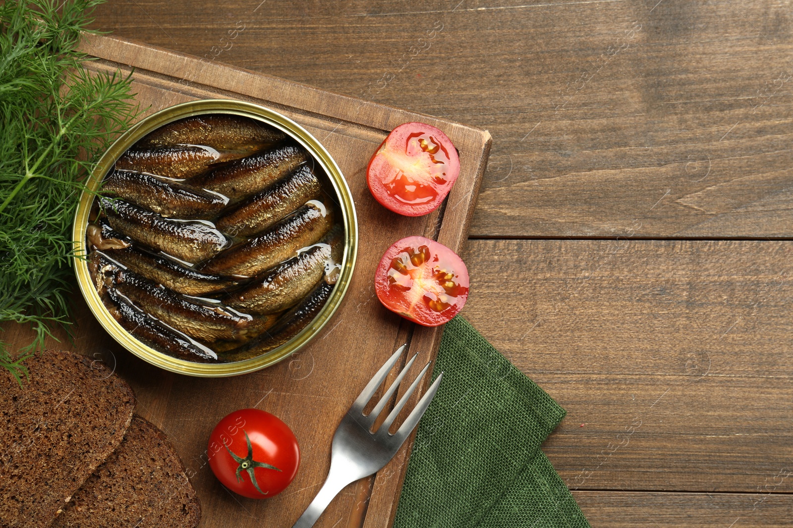 Photo of Tin can with tasty sprats served on wooden table, flat lay. Space for text