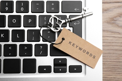 Laptop, vintage key and tag with word KEYWORDS on wooden table, top view