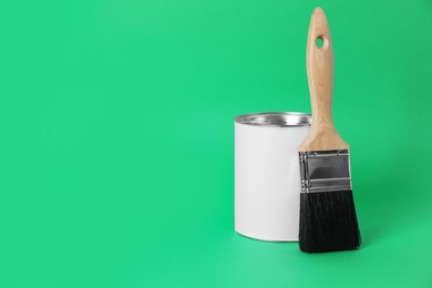 Can of orange paint and brush on green background. Space for text