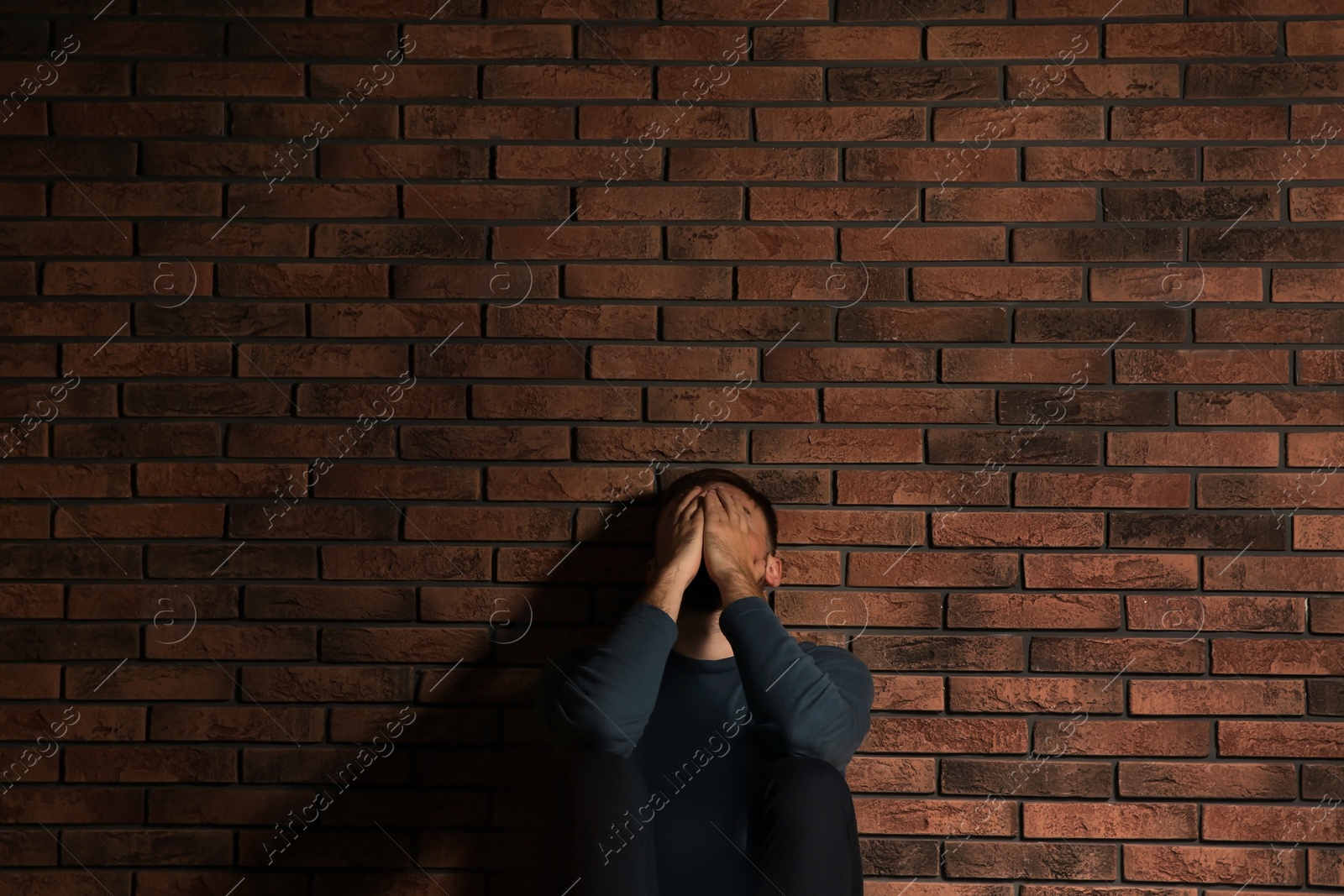Photo of Depressed young man sitting near brick wall