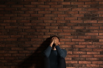 Photo of Depressed young man sitting near brick wall