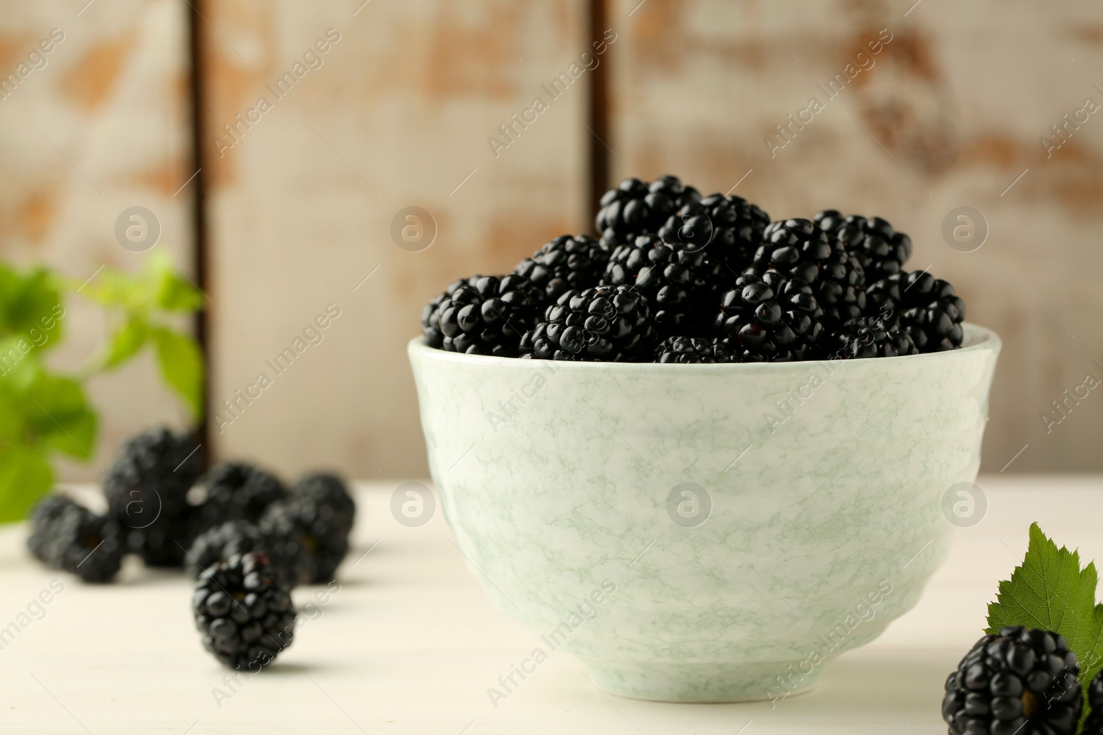 Photo of Bowl with fresh ripe blackberries on white table, closeup