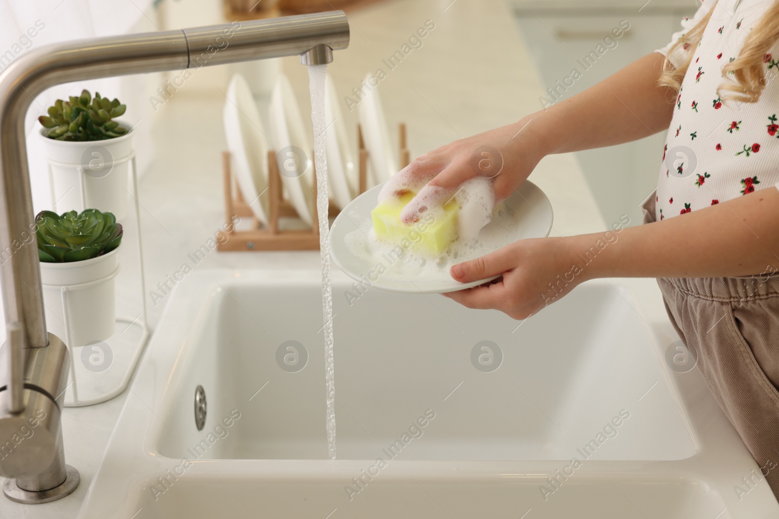 Photo of Little girl washing plate above sink in kitchen, closeup