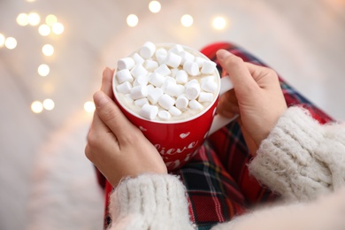 Photo of Woman holding cup of hot drink with marshmallows indoors, closeup. Magic Christmas atmosphere