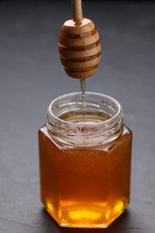 Photo of Pouring sweet honey from dipper into jar at grey table, closeup