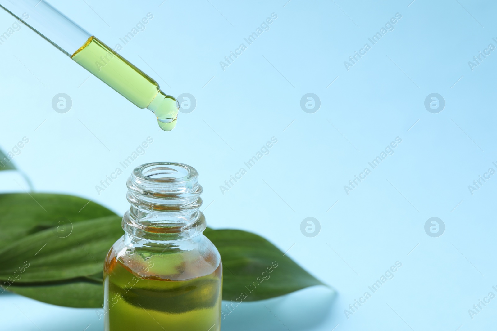 Photo of Dripping cosmetic oil from pipette into bottle on light blue background, closeup. Space for text