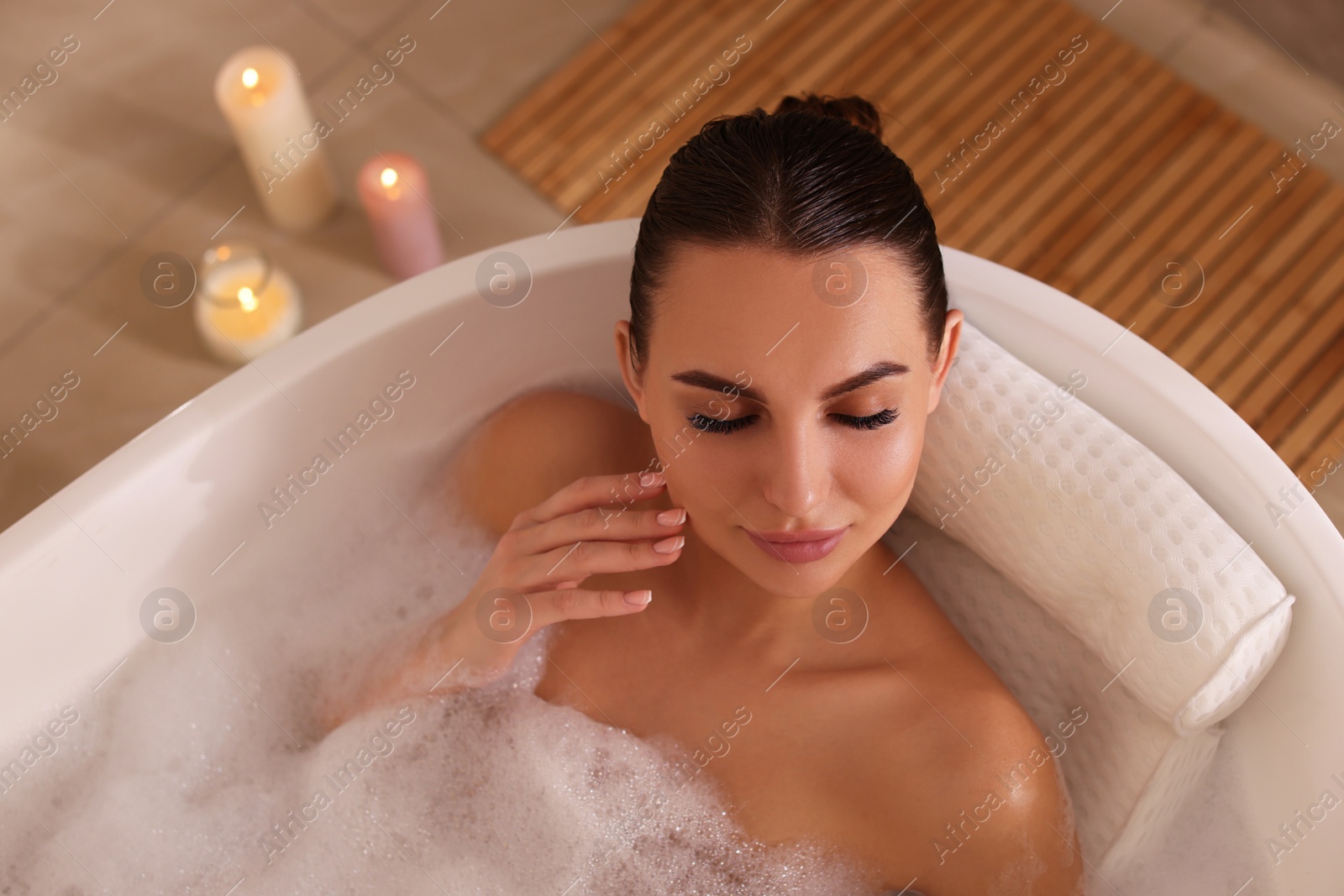 Photo of Young woman using pillow while enjoying bubble bath indoors, above view