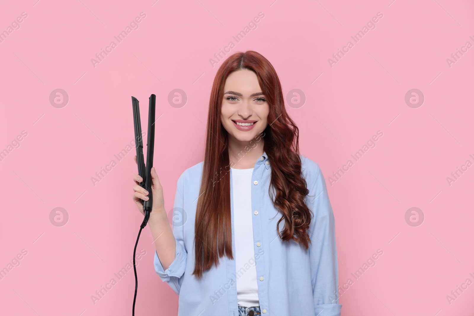 Photo of Beautiful woman with hair iron on pink background