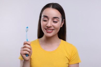 Happy young woman holding plastic toothbrush on white background