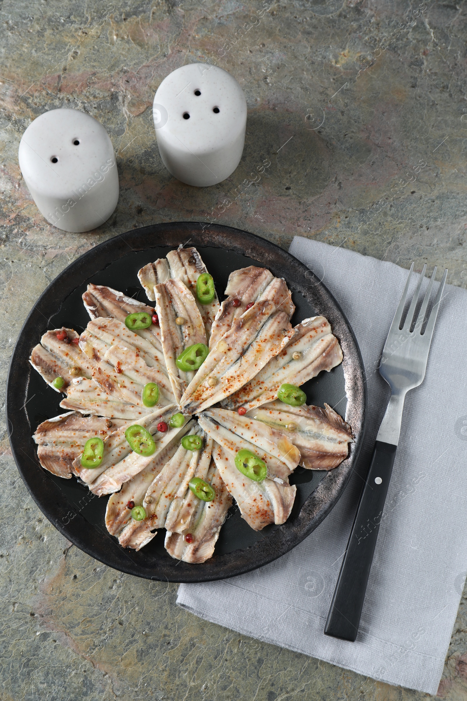 Photo of Tasty pickled anchovies with spices and fork on textured table, flat lay