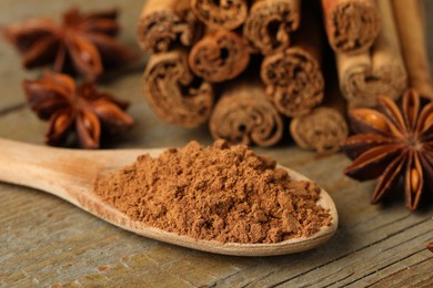 Photo of Spoon with cinnamon powder, sticks and star anise on wooden table, closeup