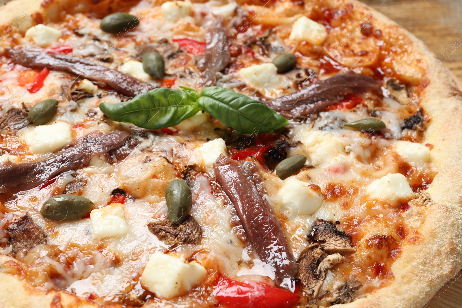 Photo of Tasty pizza with anchovies, basil and olives on wooden table, closeup