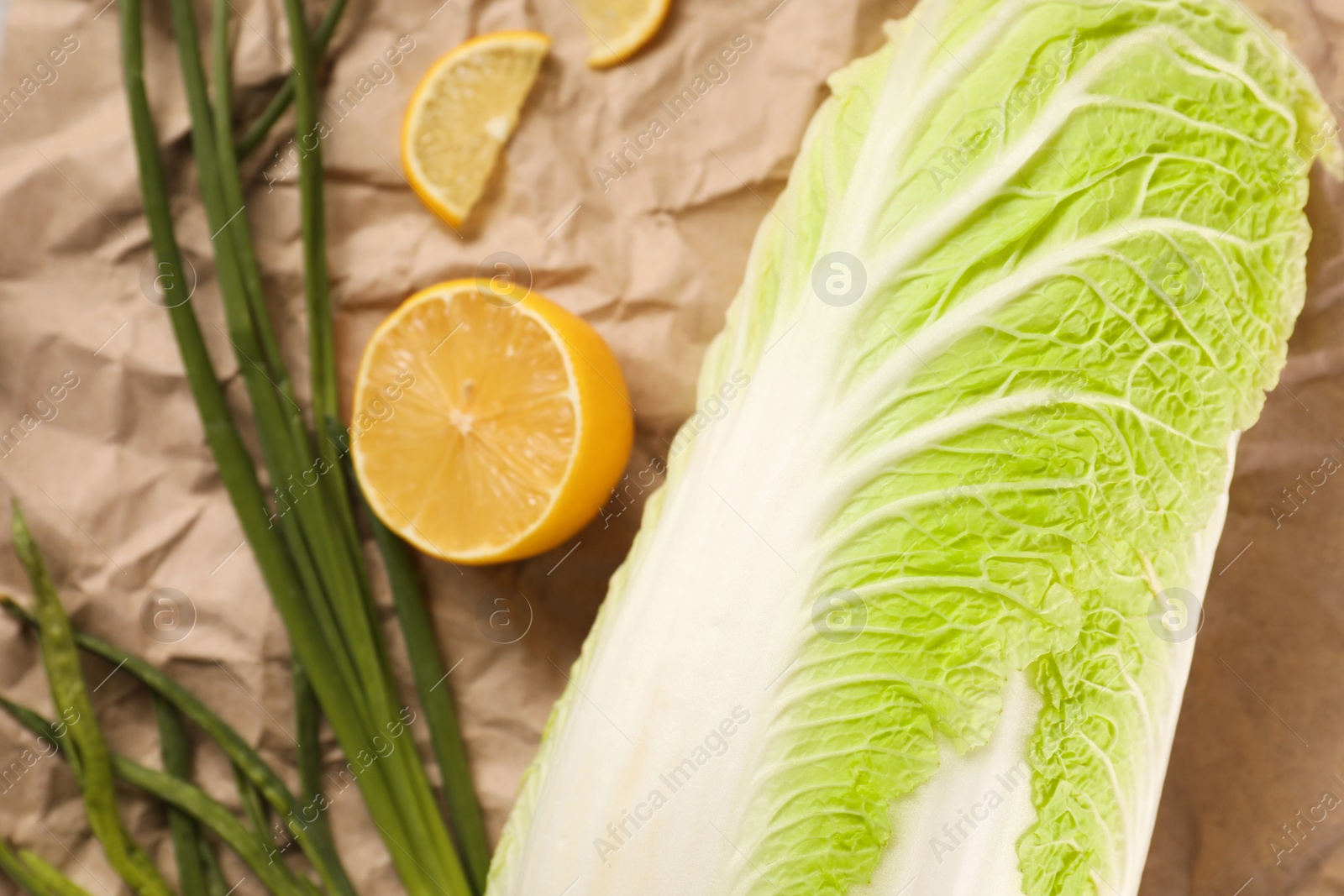 Photo of Fresh Chinese cabbage, lemon and green onion on kraft paper, closeup